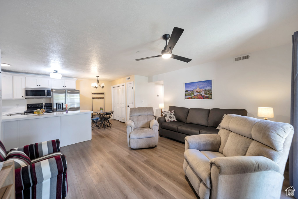 Living area featuring light wood finished floors, a ceiling fan, and a chandelier