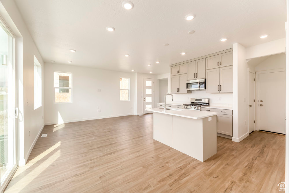 Kitchen featuring stainless steel microwave, range, a center island with sink, light wood-style flooring, and light countertops