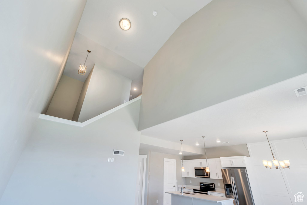 Detailed view of stainless steel appliances, light countertops, white cabinets, a center island with sink, and pendant lighting