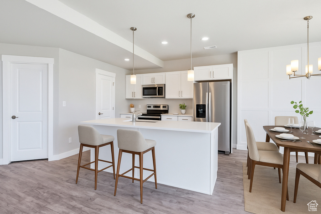 Kitchen with stainless steel appliances, a chandelier, a kitchen island with sink, light wood-style floors, and recessed lighting