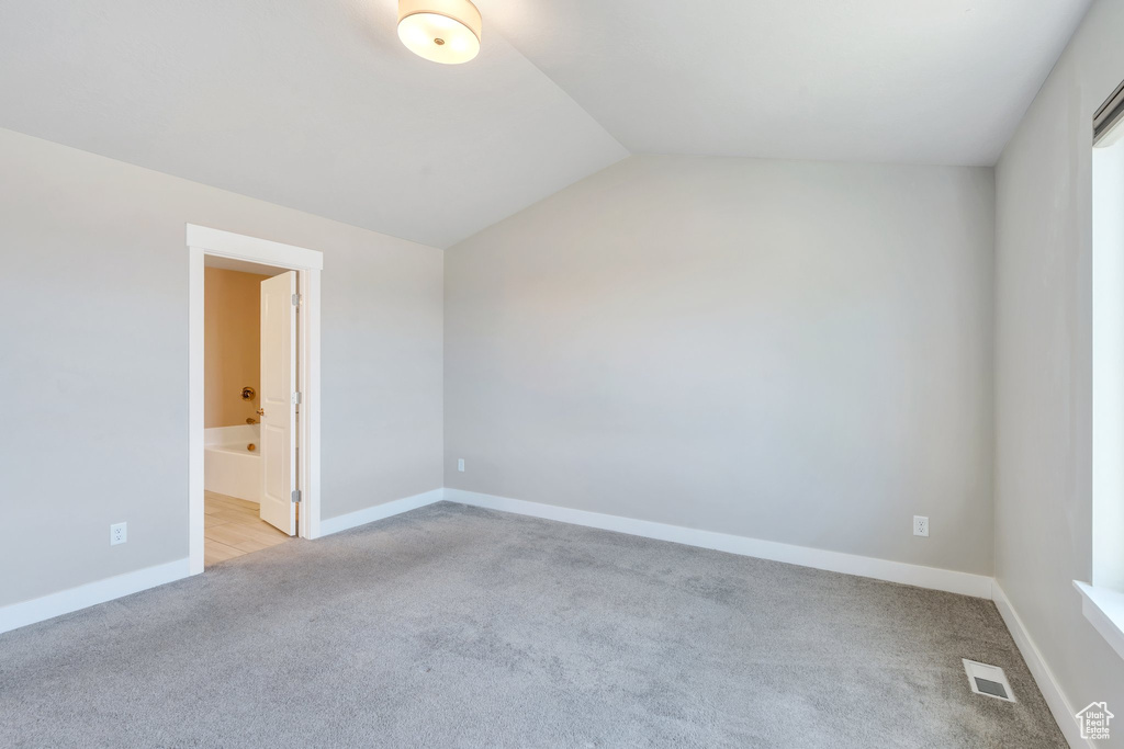 Unfurnished bedroom with light carpet, vaulted ceiling, baseboards, and ensuite bathroom
