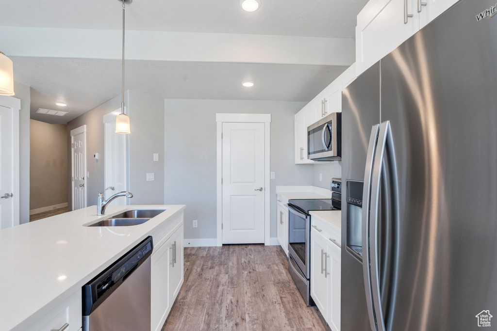 Kitchen featuring stainless steel appliances, a sink, light countertops, white cabinets, and pendant lighting