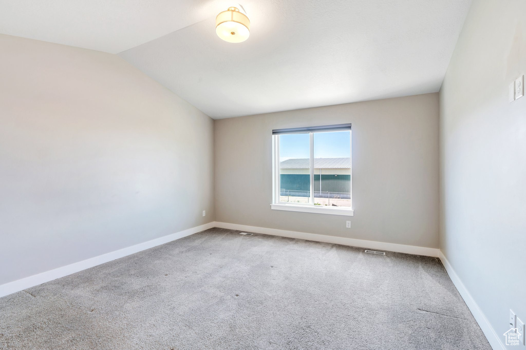 Carpeted spare room with vaulted ceiling and baseboards