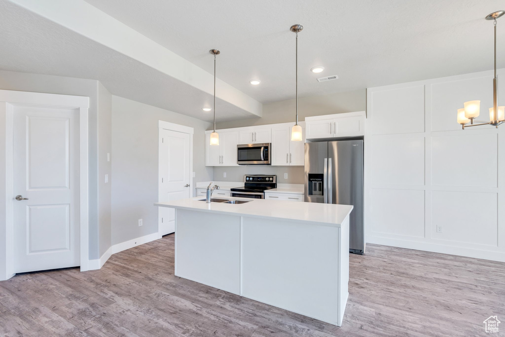 Kitchen with stainless steel appliances, white cabinets, light countertops, a kitchen island with sink, and a chandelier