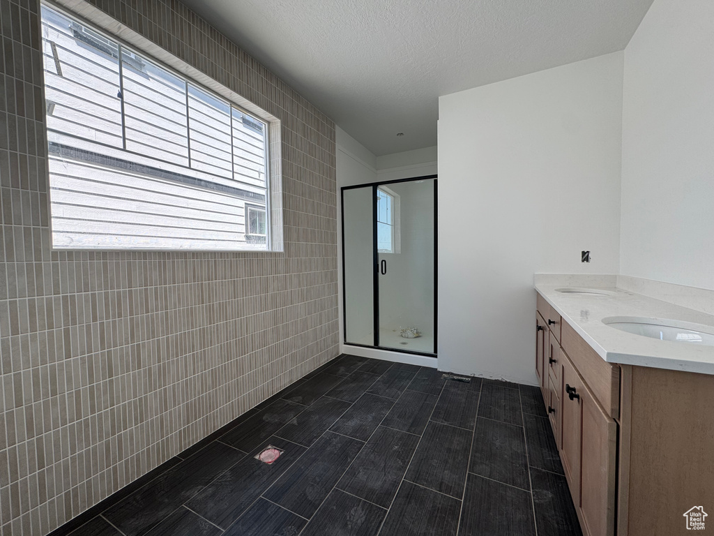 Bathroom featuring a stall shower, double vanity, and tile walls