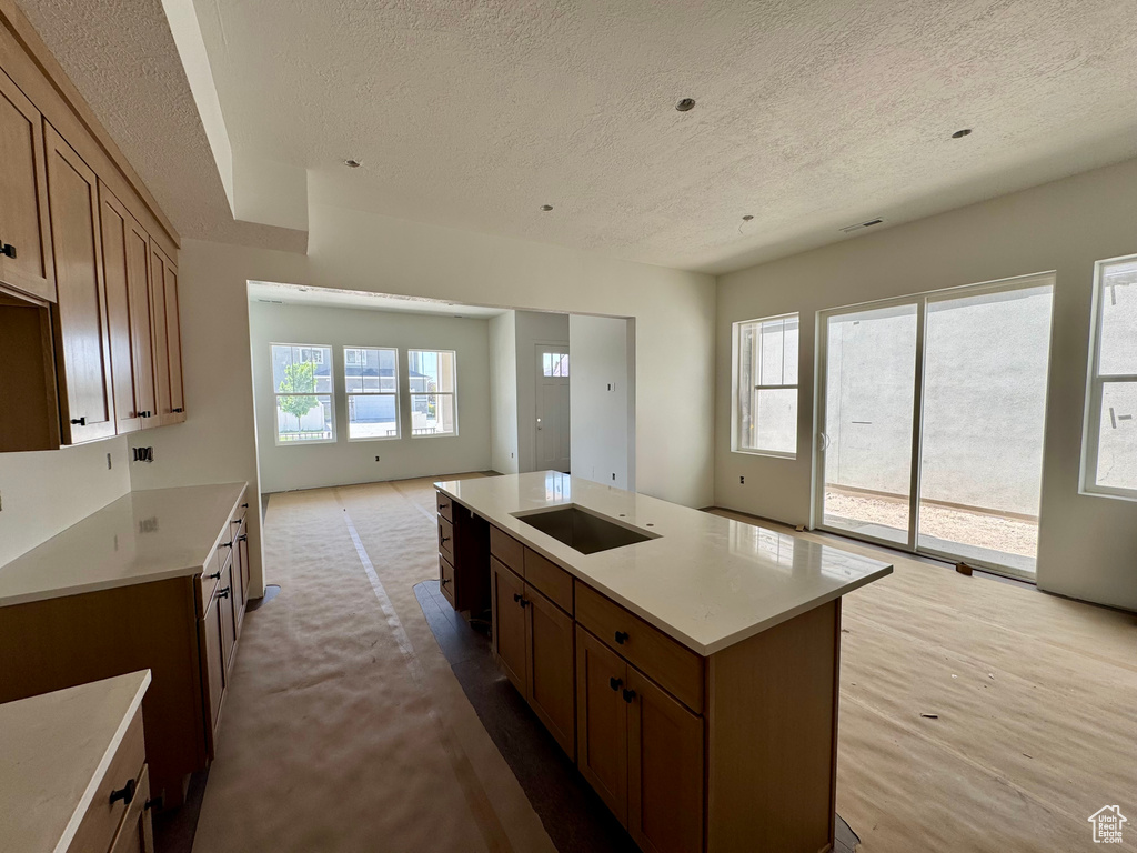 Kitchen featuring a textured ceiling, light countertops, black electric stovetop, open floor plan, and brown cabinetry