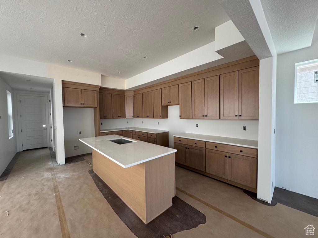Kitchen featuring a textured ceiling, a center island, brown cabinets, and concrete flooring