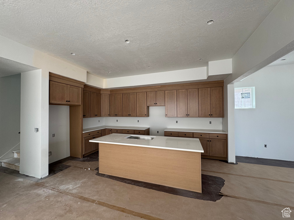 Kitchen with concrete floors, a kitchen island, a textured ceiling, brown cabinets, and light countertops