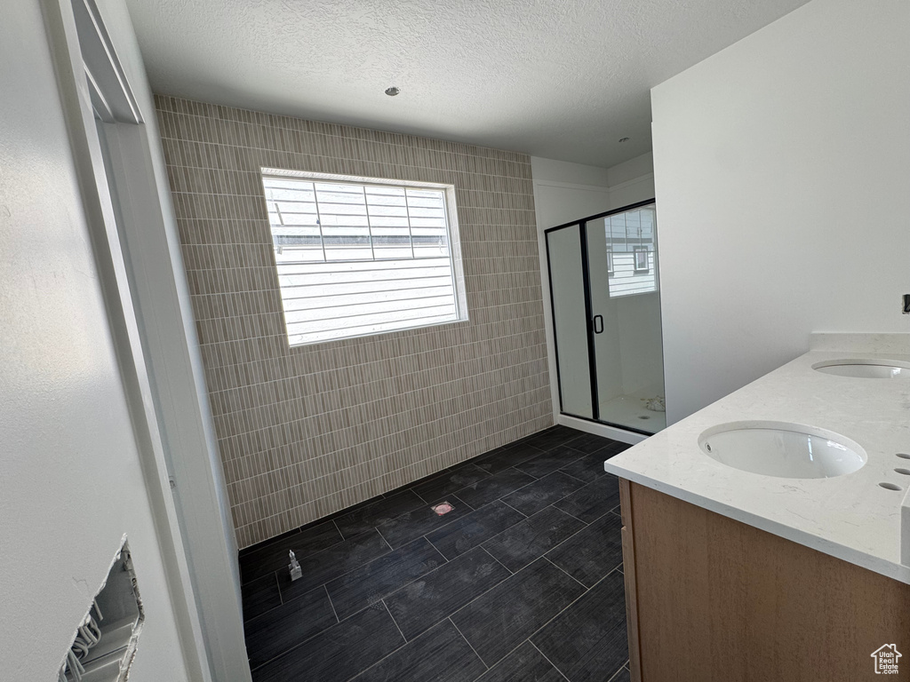 Bathroom with a stall shower, double vanity, tile walls, tile patterned flooring, and a textured ceiling