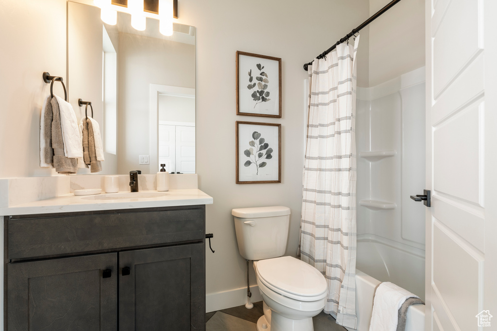 Bathroom featuring baseboards, toilet, vanity, and shower / tub combo