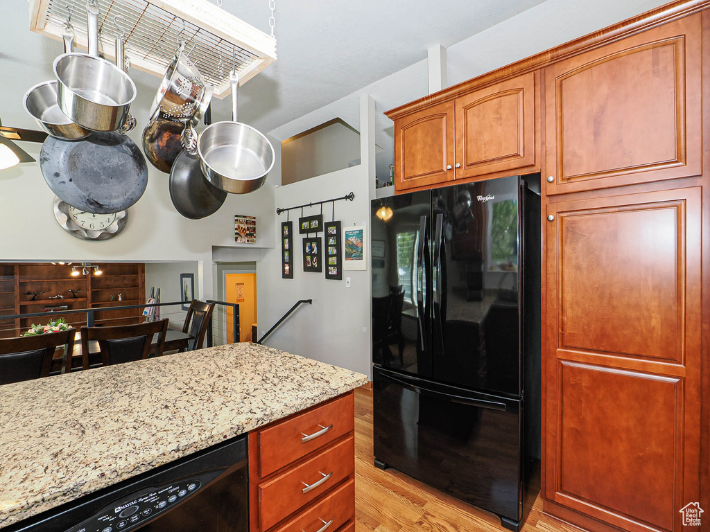 Kitchen featuring black appliances, light wood finished floors, light stone counters, and brown cabinetry
