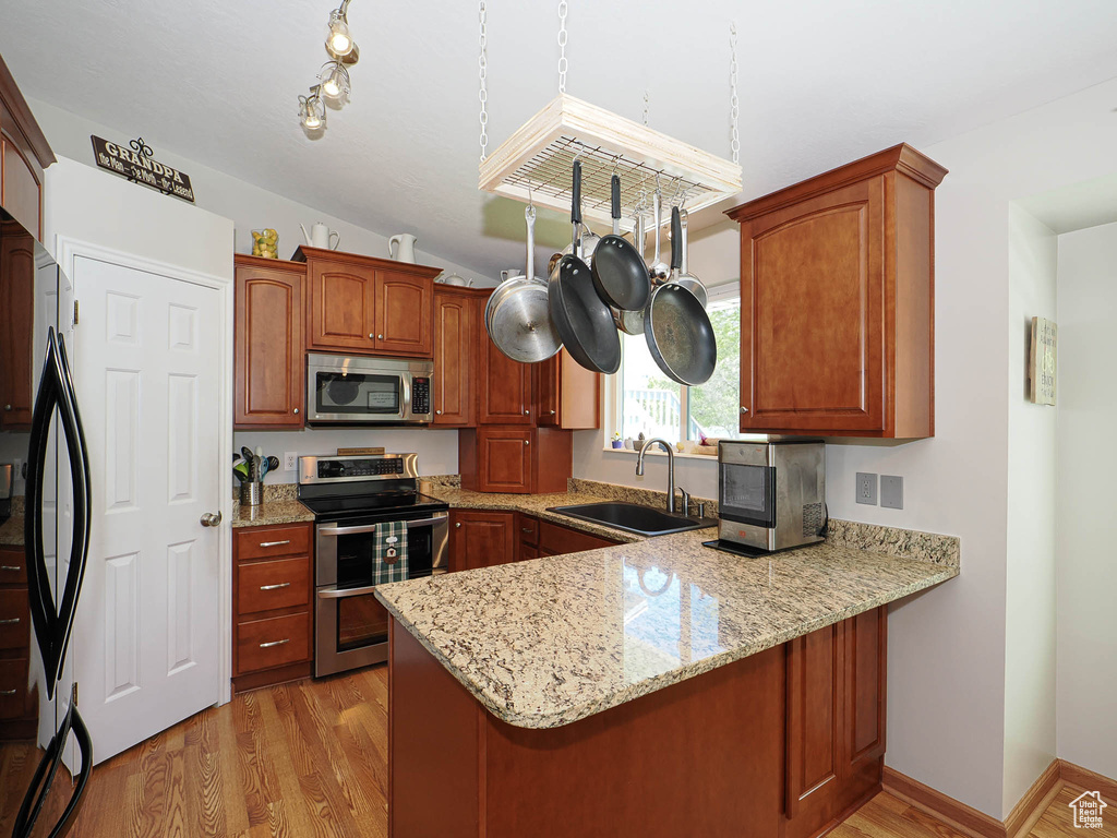 Kitchen featuring stainless steel appliances, a peninsula, a sink, light stone counters, and light wood finished floors