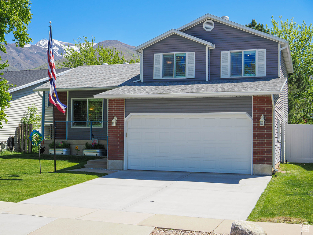 View of front of house with a front yard, a mountain view, an attached garage, concrete driveway, and brick siding