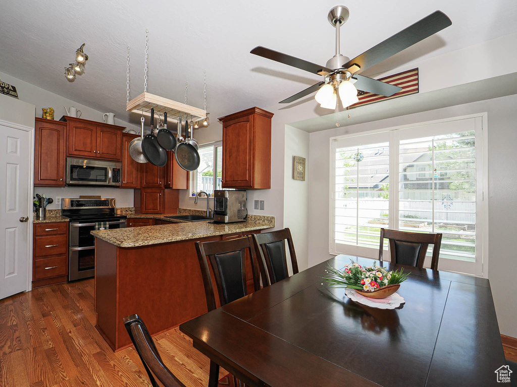Kitchen with appliances with stainless steel finishes, dark wood-style flooring, ceiling fan, a peninsula, and light stone counters