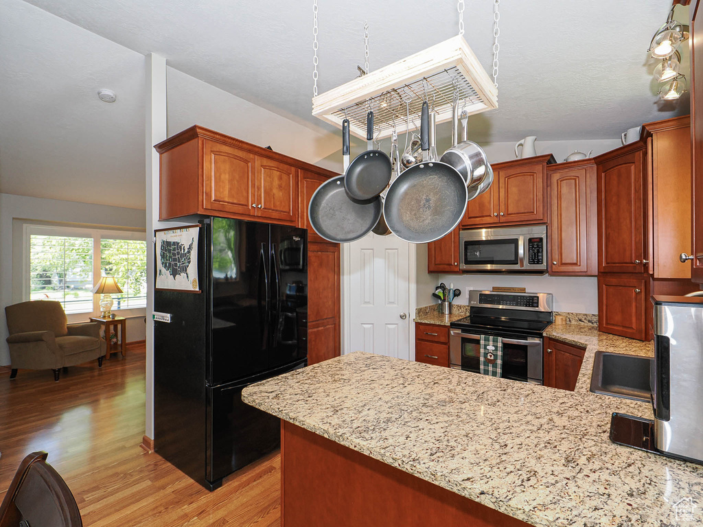 Kitchen with stainless steel appliances, a peninsula, light wood-style floors, and light stone countertops