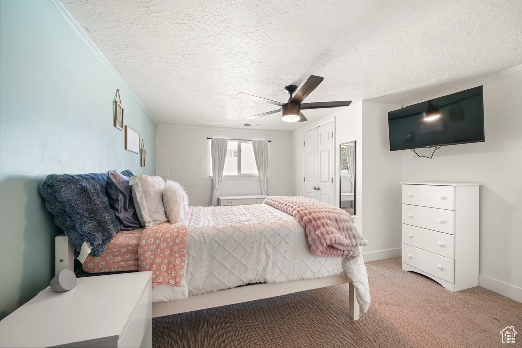 Bedroom with light carpet, a textured ceiling, a closet, a ceiling fan, and baseboards