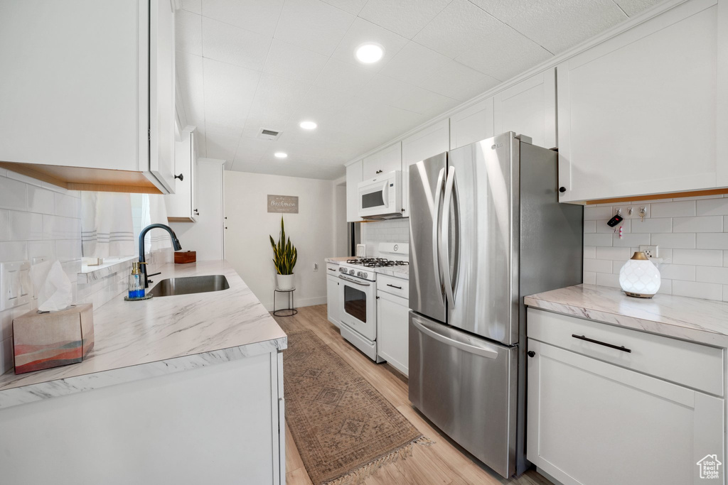 Kitchen with white appliances, a sink, backsplash, light wood-style floors, and white cabinetry