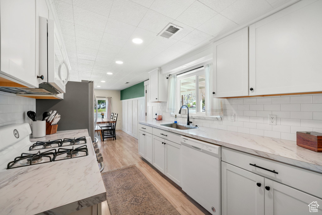 Kitchen with a sink, white appliances, light wood-style flooring, white cabinetry, and recessed lighting