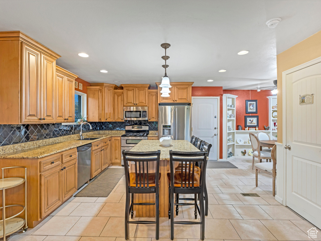 Kitchen featuring appliances with stainless steel finishes, a sink, light stone counters, a breakfast bar area, and decorative backsplash