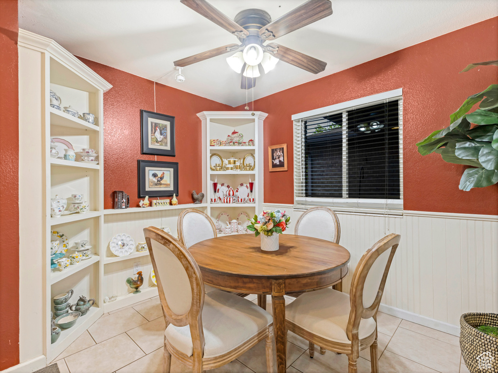 Dining space featuring a ceiling fan, tile patterned flooring, a wainscoted wall, and a textured wall