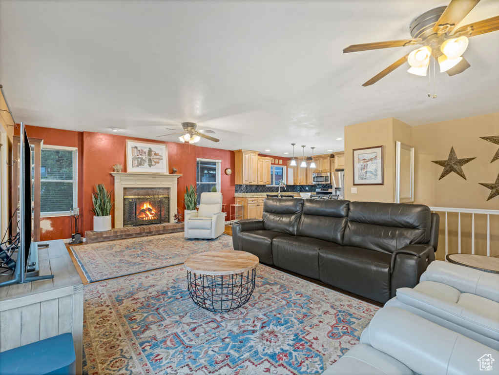 Living area with ceiling fan, a brick fireplace, and healthy amount of natural light