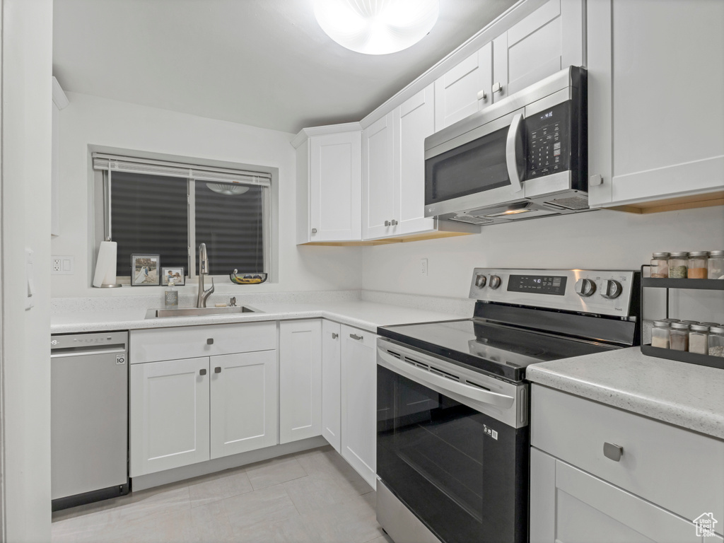 Kitchen with appliances with stainless steel finishes, a sink, white cabinets, and light countertops