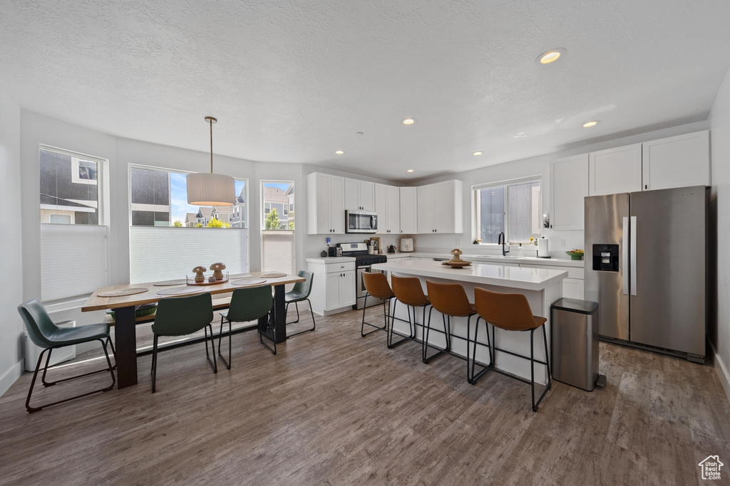 Kitchen with appliances with stainless steel finishes, a breakfast bar area, white cabinetry, a center island, and dark wood-type flooring