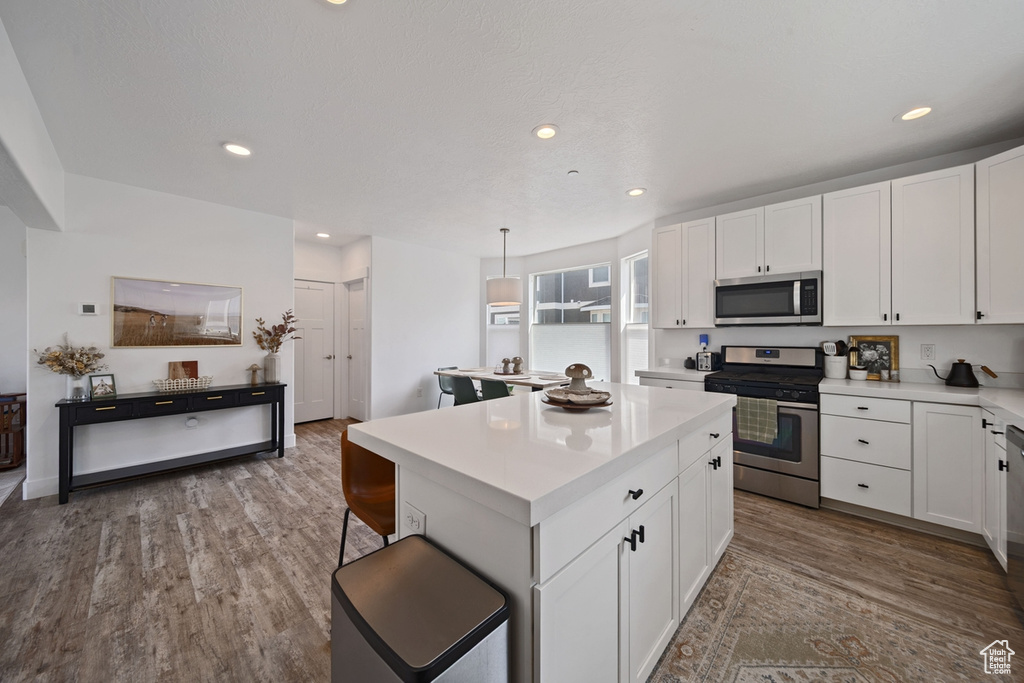Kitchen featuring appliances with stainless steel finishes, a kitchen island, light countertops, white cabinetry, and wood finished floors