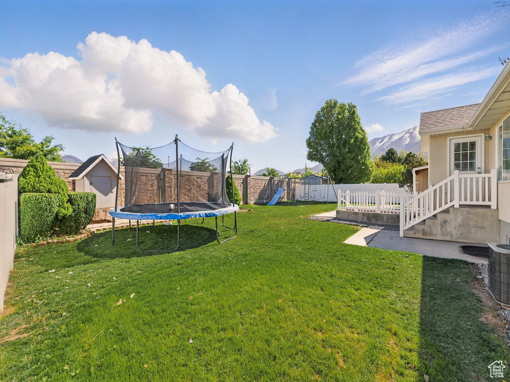 View of yard featuring a trampoline, a playground, a storage shed, an outbuilding, and central AC