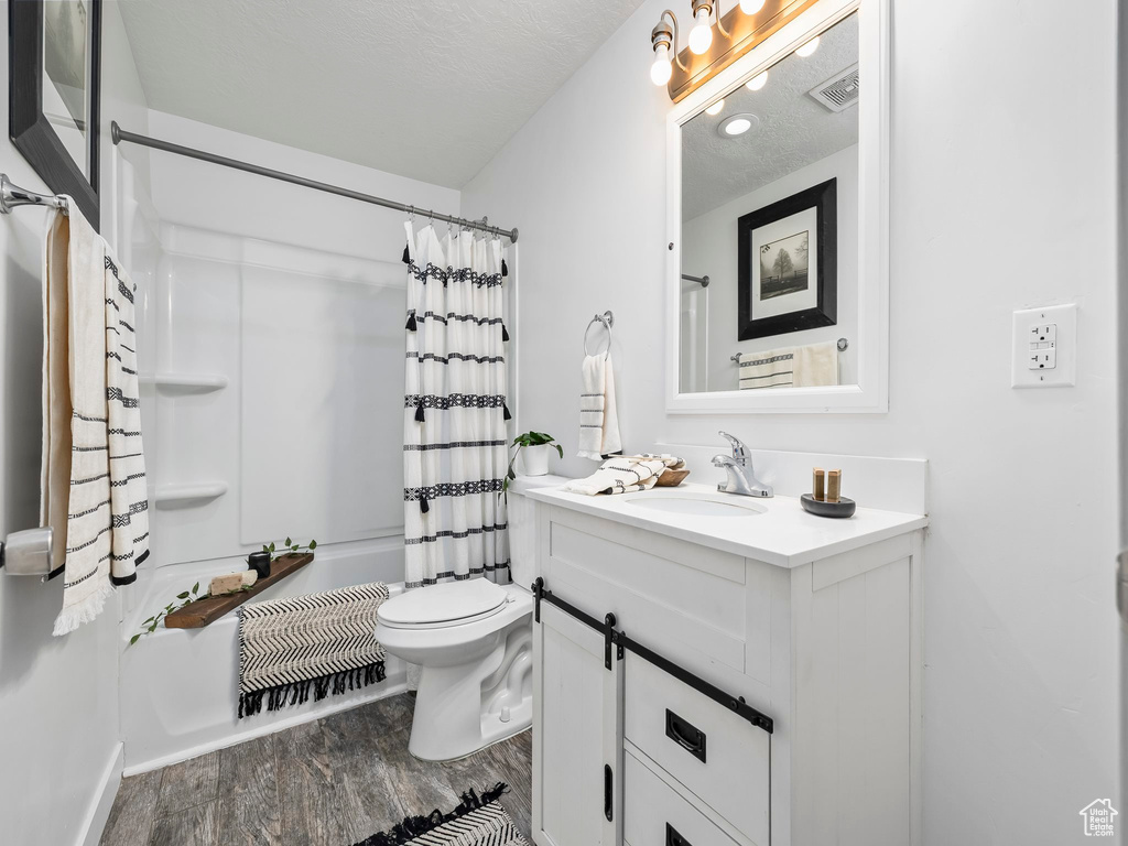 Bathroom with wood finished floors, toilet, vanity, shower / tub combo, and baseboards