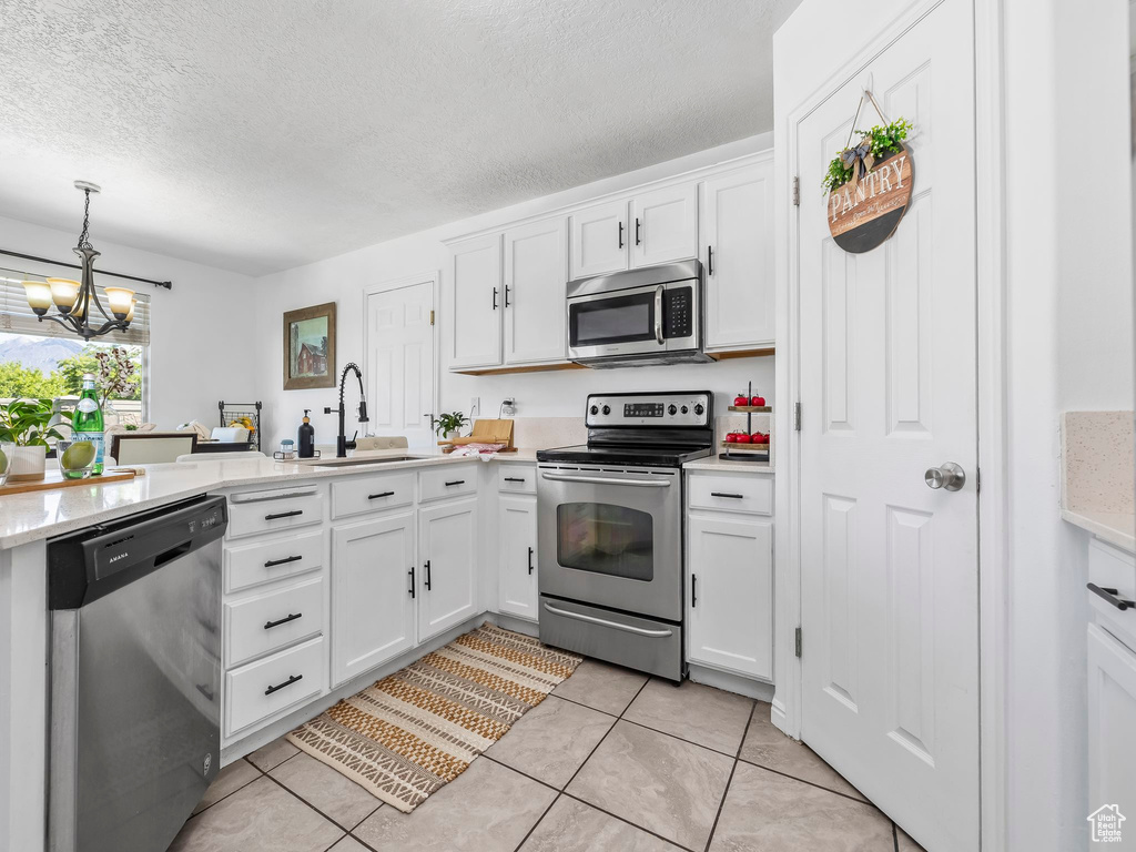 Kitchen with stainless steel appliances, a chandelier, a textured ceiling, light tile patterned flooring, and a sink