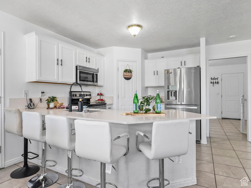 Kitchen with appliances with stainless steel finishes, a peninsula, white cabinets, light tile patterned floors, and a textured ceiling