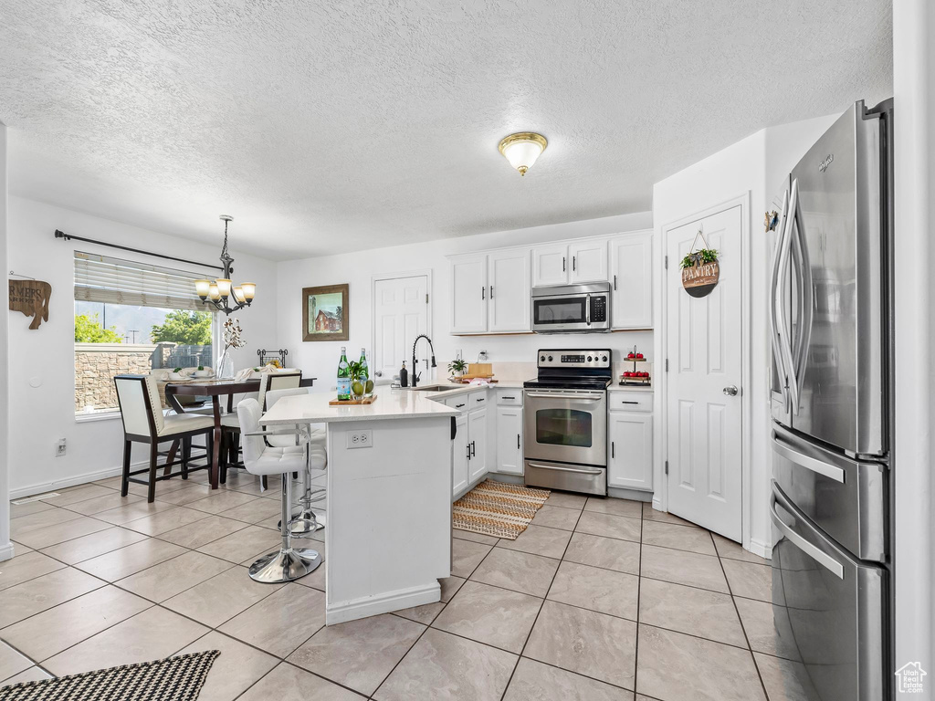 Kitchen featuring stainless steel appliances, a peninsula, a sink, a chandelier, and white cabinetry