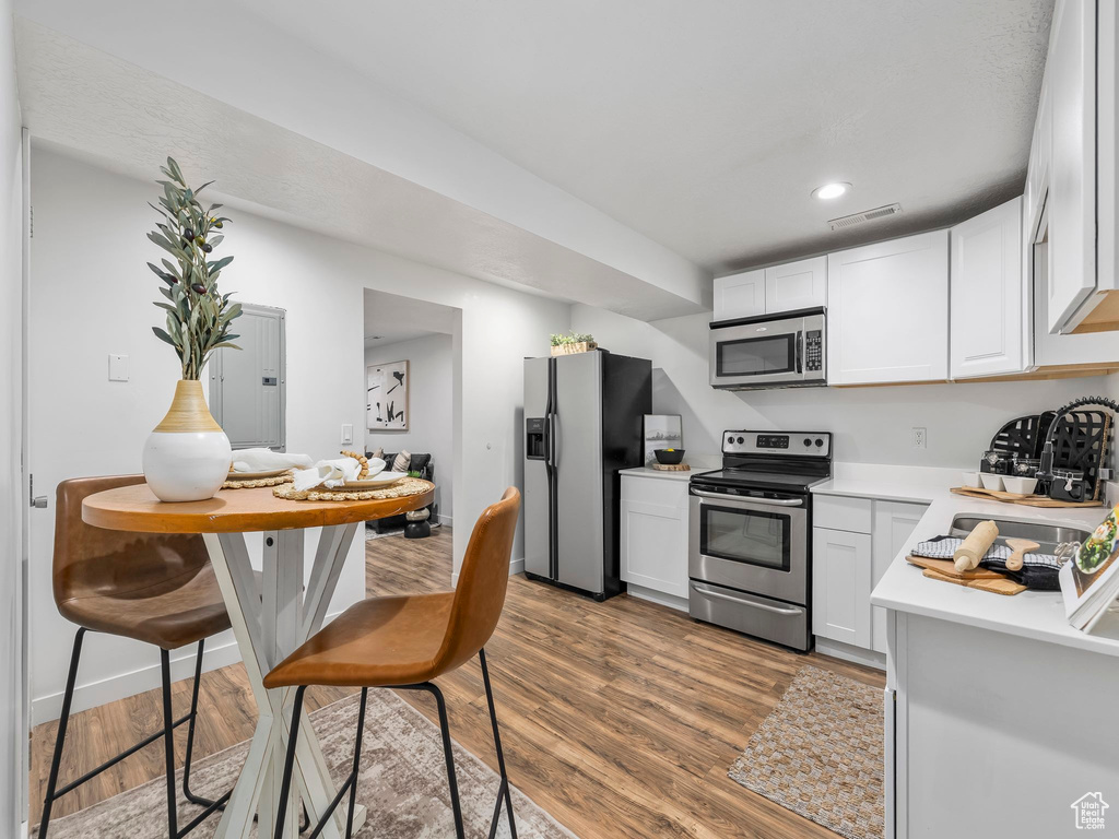 Kitchen featuring stainless steel appliances, light countertops, wood finished floors, white cabinetry, and recessed lighting
