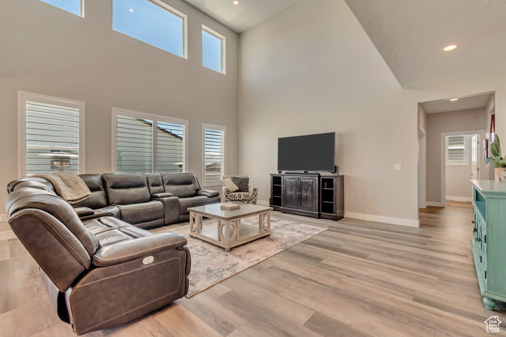 Living area featuring baseboards, light wood-type flooring, a towering ceiling, and recessed lighting