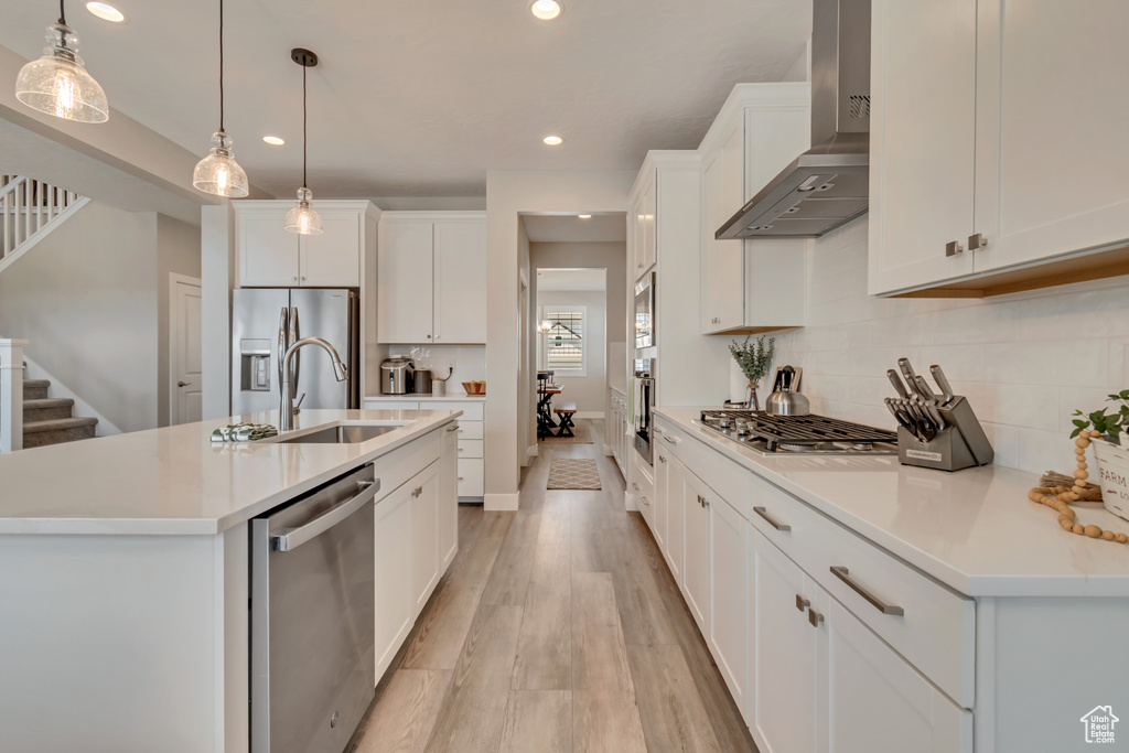 Kitchen with wall chimney range hood, appliances with stainless steel finishes, a sink, recessed lighting, and light wood-style flooring