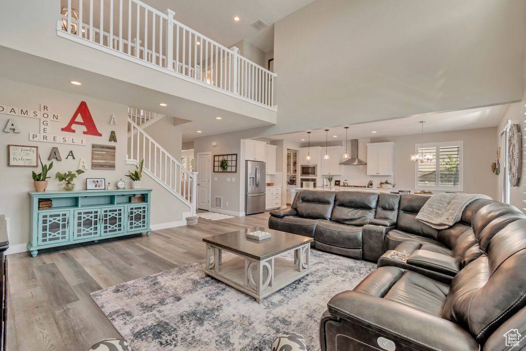 Living room featuring light wood-type flooring, stairway, a high ceiling, baseboards, and a chandelier