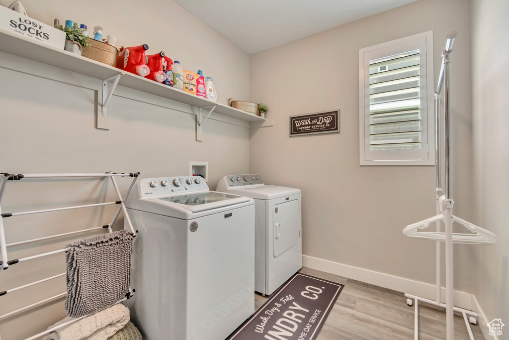 Clothes washing area with washing machine and clothes dryer, light wood finished floors, and baseboards