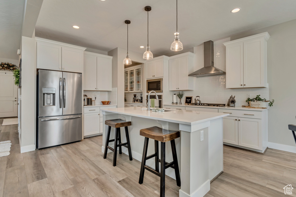Kitchen featuring stainless steel refrigerator with ice dispenser, wall chimney exhaust hood, built in microwave, a sink, and recessed lighting