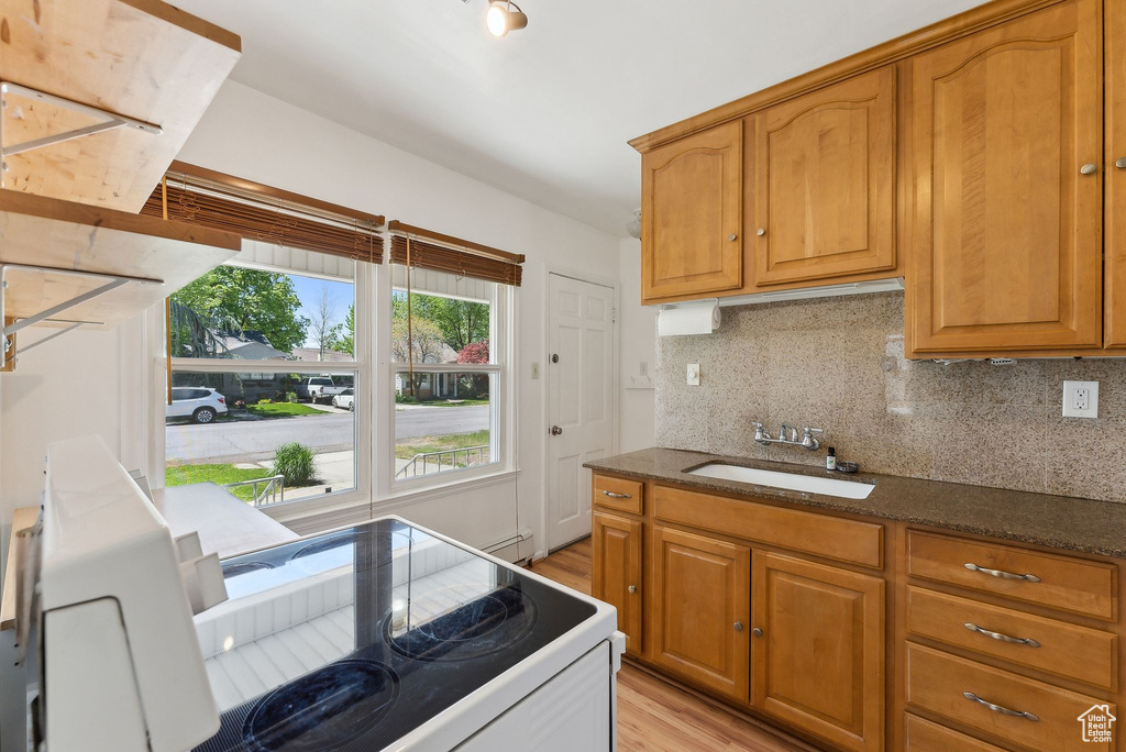 Kitchen featuring a sink, light wood-style floors, tasteful backsplash, dark stone counters, and brown cabinets