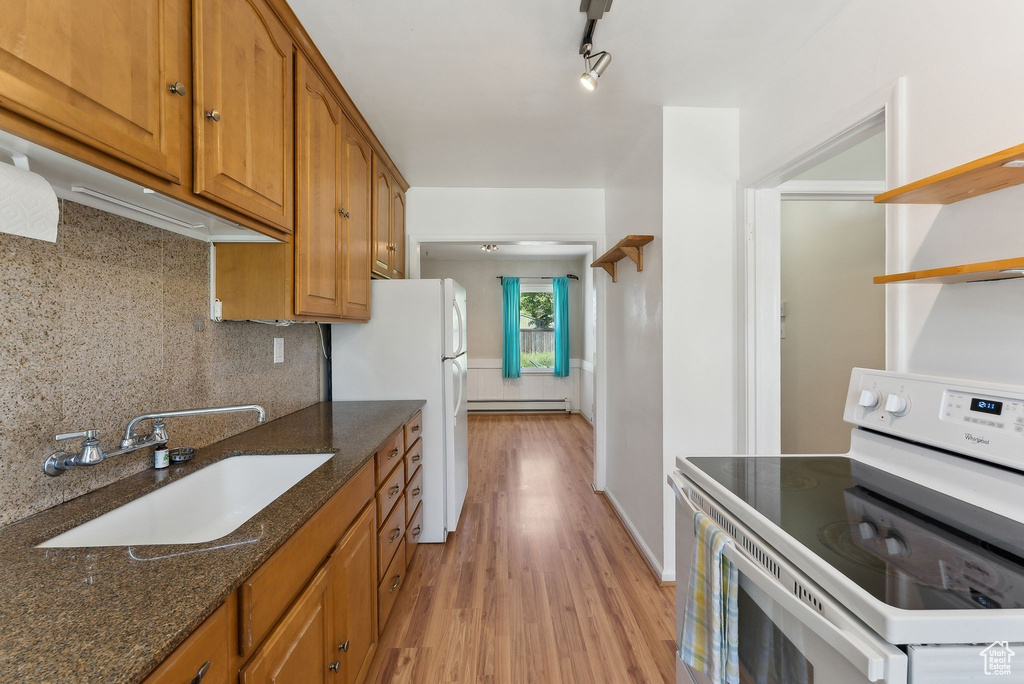 Kitchen featuring white appliances, a sink, baseboard heating, light wood finished floors, and dark stone countertops