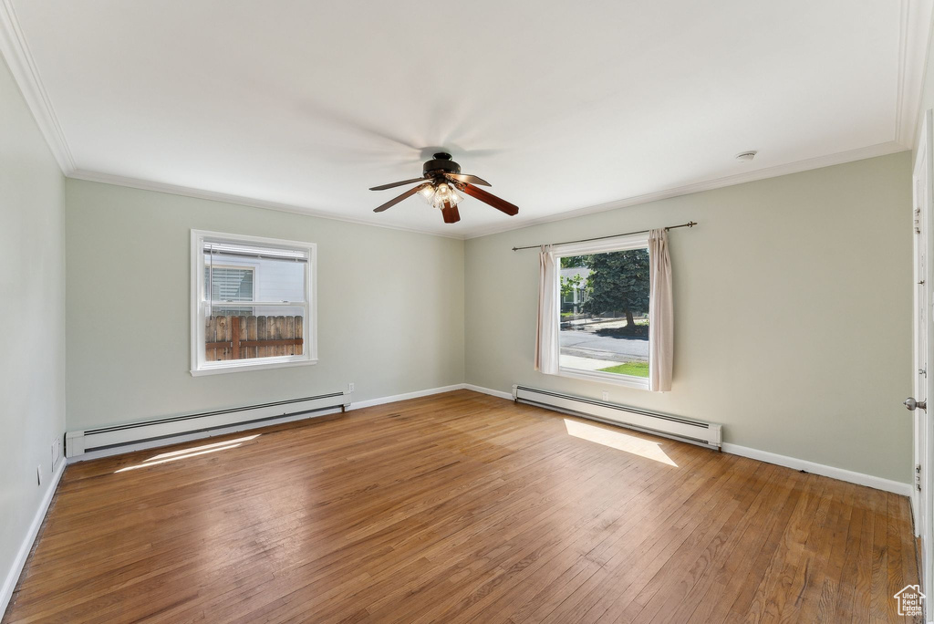 Unfurnished room with baseboard heating, a ceiling fan, ornamental molding, hardwood / wood-style flooring, and baseboards