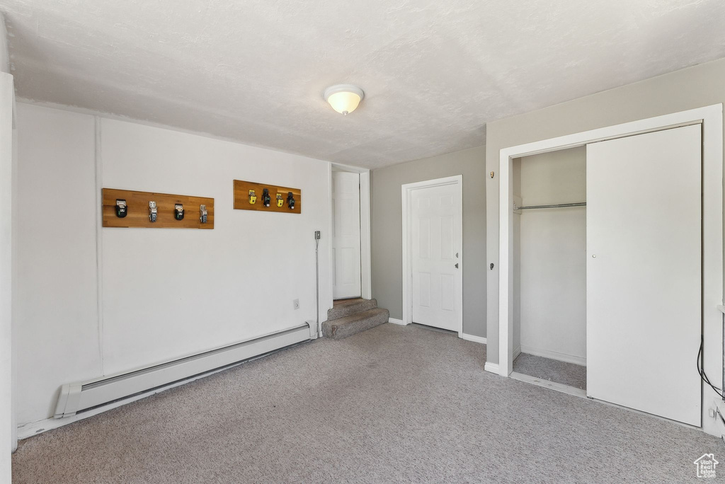Unfurnished bedroom with baseboard heating, carpet flooring, a closet, and baseboards