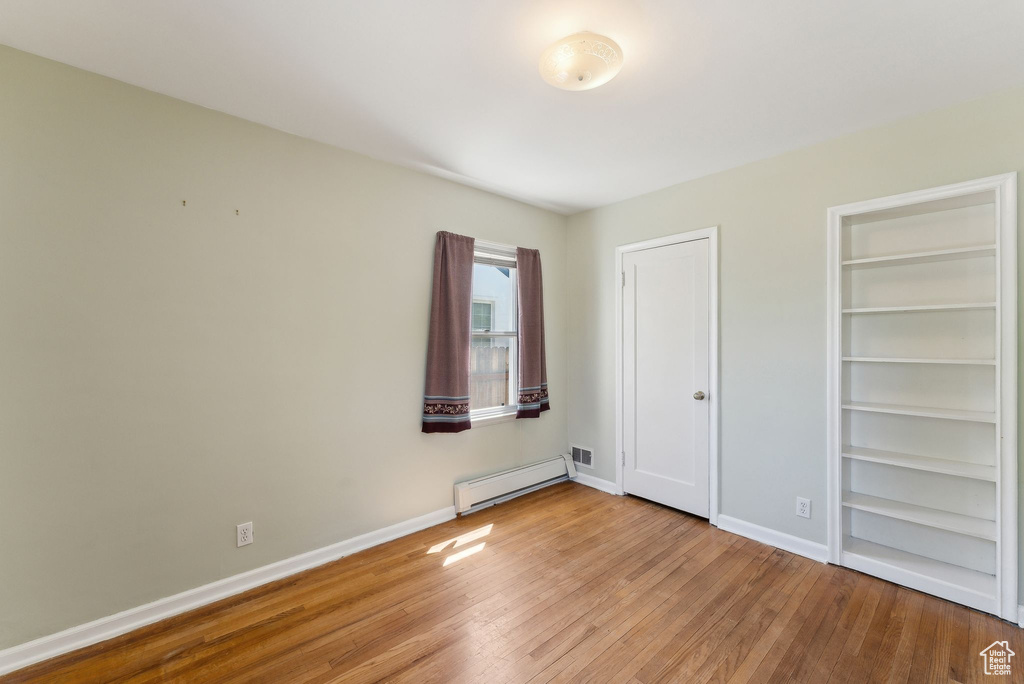 Unfurnished bedroom with a baseboard radiator, wood finished floors, and baseboards