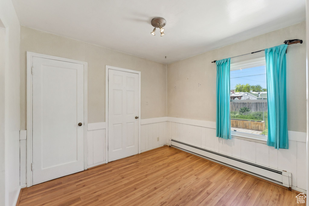 Spare room with a baseboard heating unit, light wood-style floors, and a wainscoted wall