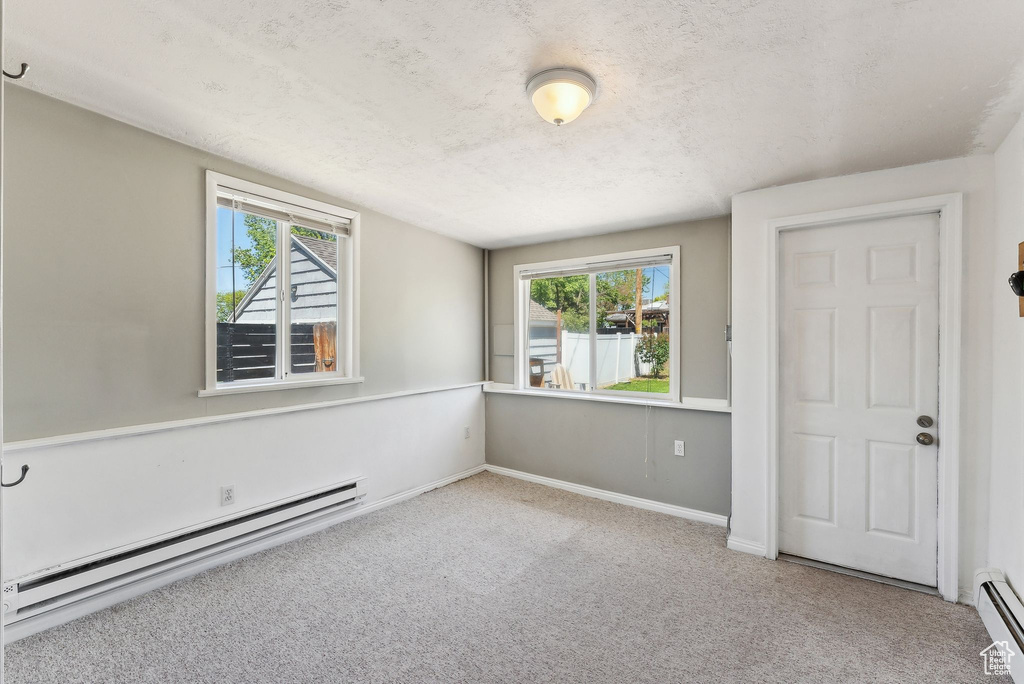 Spare room with a baseboard heating unit, a baseboard radiator, carpet, plenty of natural light, and a textured ceiling