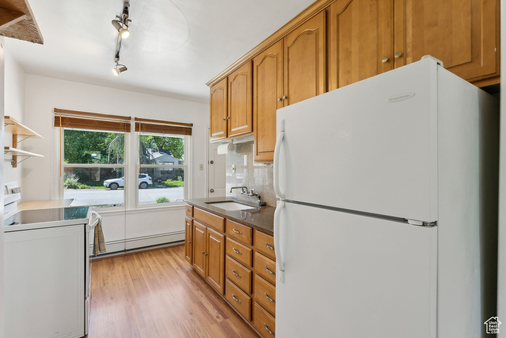 Kitchen featuring freestanding refrigerator, a baseboard heating unit, a sink, light wood-style floors, and brown cabinetry