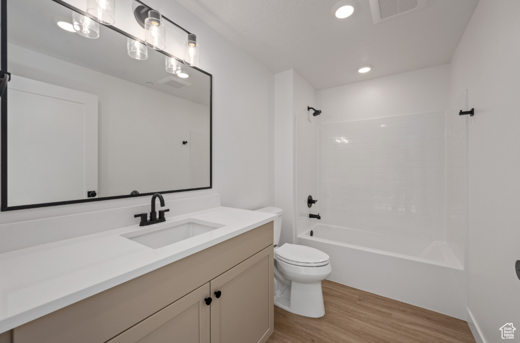 Bathroom with toilet, wood finished floors, washtub / shower combination, visible vents, and vanity