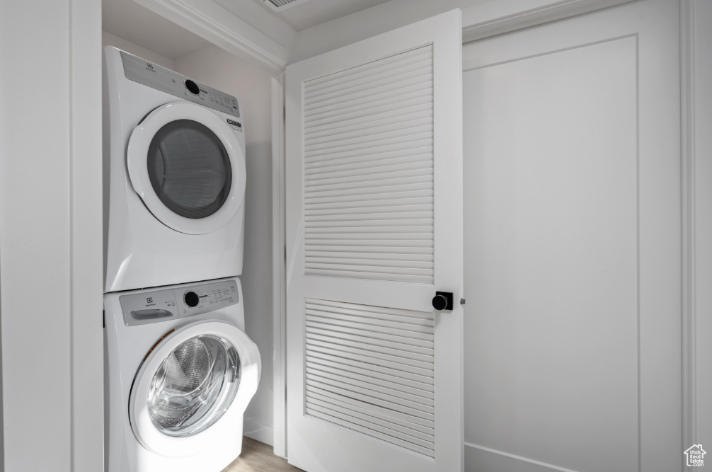 Washroom with laundry area, stacked washer and clothes dryer, and light wood finished floors