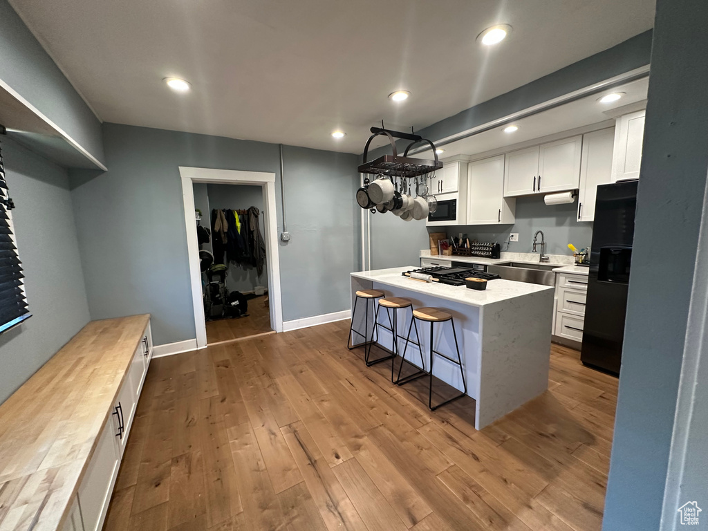 Kitchen featuring black fridge, white microwave, a center island, white cabinetry, and a breakfast bar